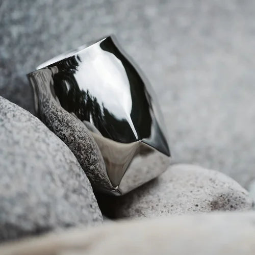 Lifestyle image of the Norlan Steel Tumbler, an outdoor whiskey vessel made of double-walled stainless steel, shown in polished steel nestled in between grey boulder rocks. 