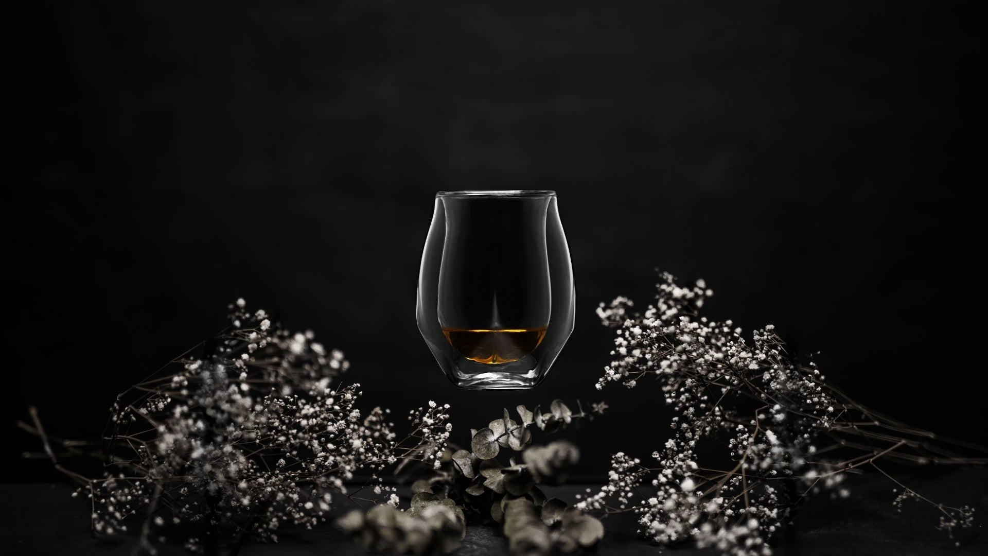 Lifestyle image of the Norlan Whisky Glass in Clear floating in the center of a white floral arrangement.